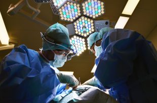 Surgeons in an operating theatre working on a patient with overhead lamps in the background
