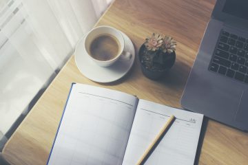 An open diary with appointments next to a cup of coffee and a laptop
